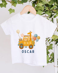 A white t-shirt with a graphic design featuring a yellow car, a giraffe, and balloons, along with the text "ONE OSCAR".