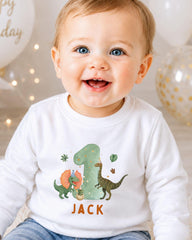 A smiling baby boy wearing a white shirt with a dinosaur graphic and the name "Jack" printed on it.