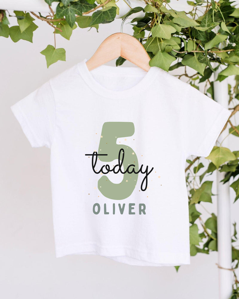 A white t-shirt with a green number 5 and the text "Today Oliver" printed on it, hanging on a wooden hanger.