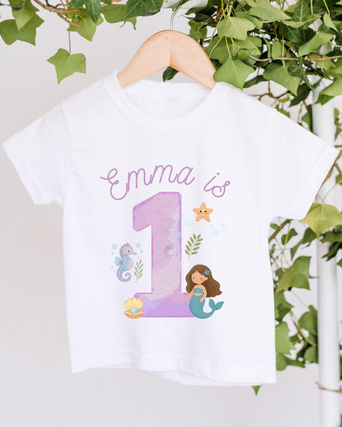 A white t-shirt with a mermaid and a number 1 printed on it, along with some marine-themed elements.