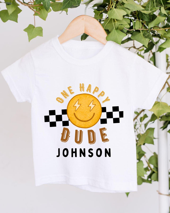 A white t-shirt with a cheerful smiley face and text printed on it, hanging on a wooden hanger.