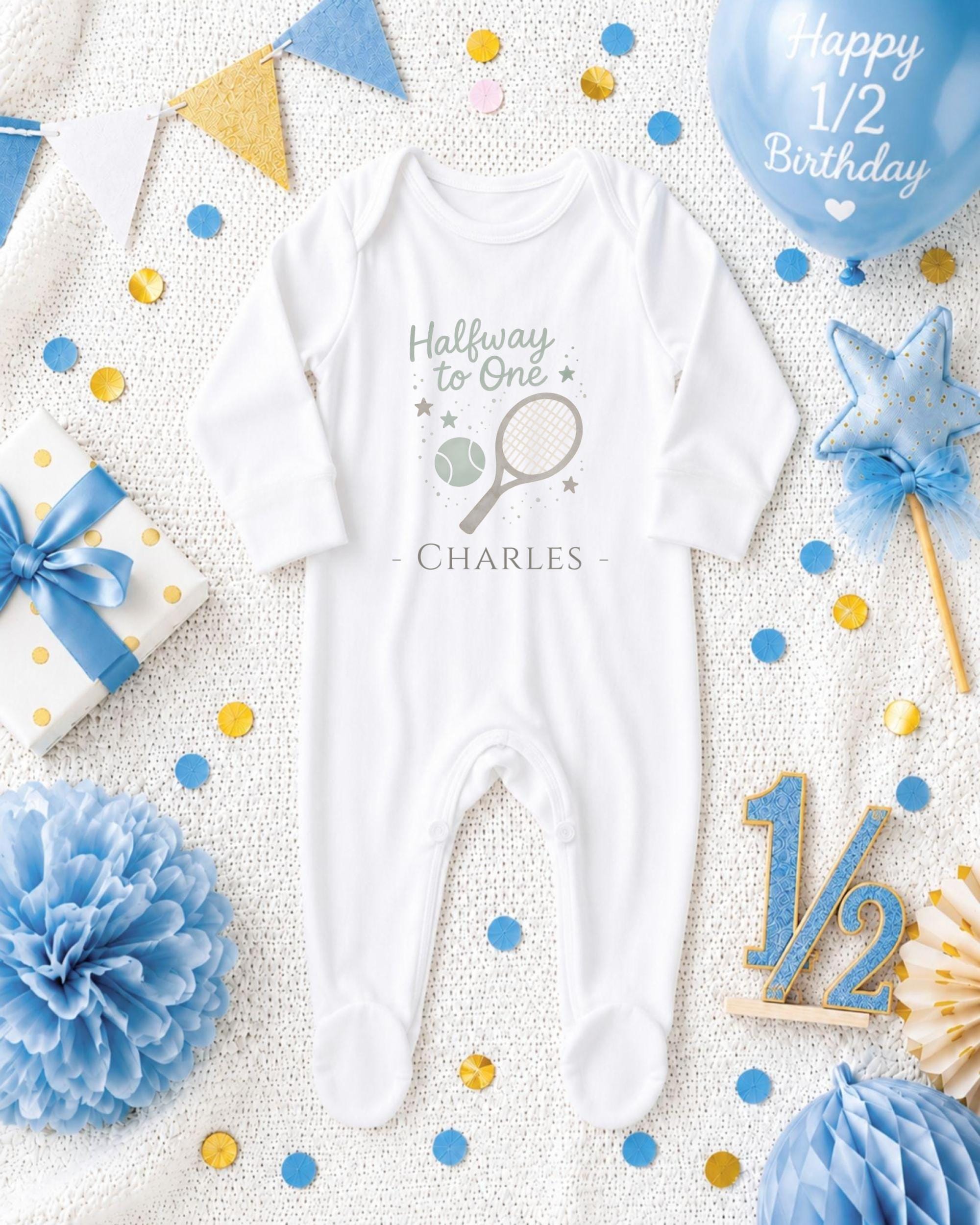 A white onesie with a tennis racket and stars on it, surrounded by confetti, a blue balloon, and other baby-related items, all arranged on a white background.
