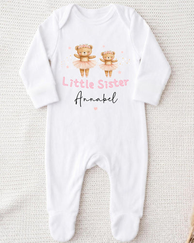 A white bodysuit with a design of two teddy bears in tutus and the text "Little Sister Annabel" printed on it.