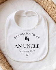 A white bib with the text "GET READY TO BE AN UNCLE In January 2028" printed on it, along with a small black footprint symbol.