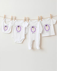 A row of white baby clothes, including onesies and bibs, hanging on a clothesline.