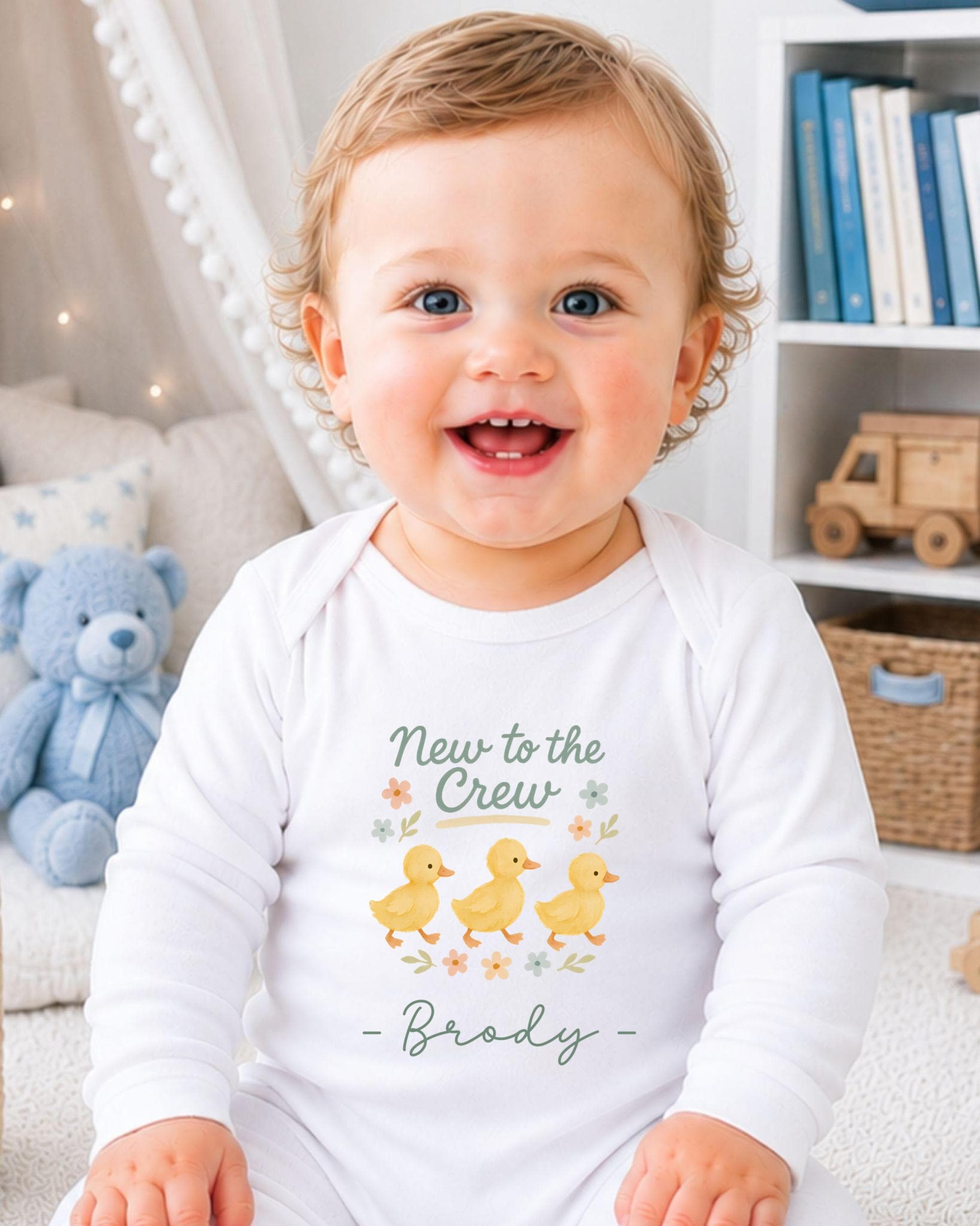 A smiling baby boy wearing a white onesie with a graphic of ducks and the text "New to the Crew - Brady" printed on it.