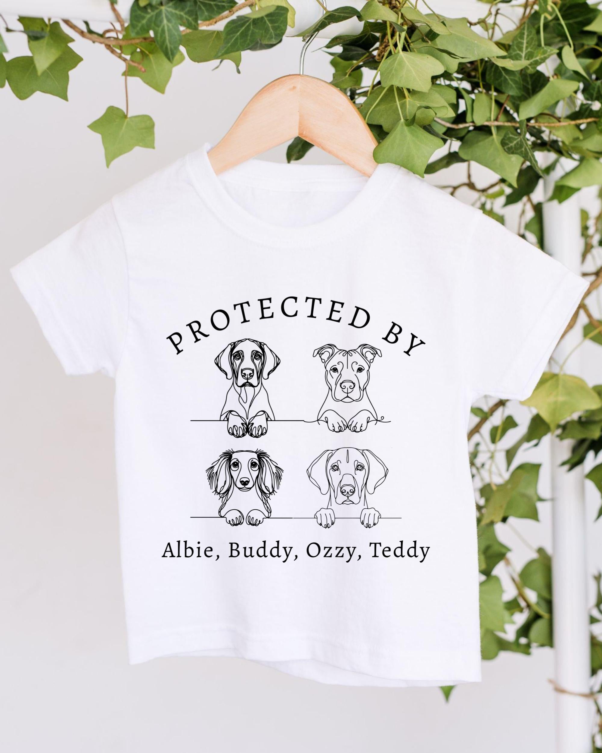 A white t-shirt with a graphic design featuring four cartoon dog illustrations and the text "PROTECTED BY Albie, Buddy, Ozzy, Teddy".