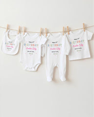 A row of four white baby clothes, including onesies and bibs, hanging on a clothesline.