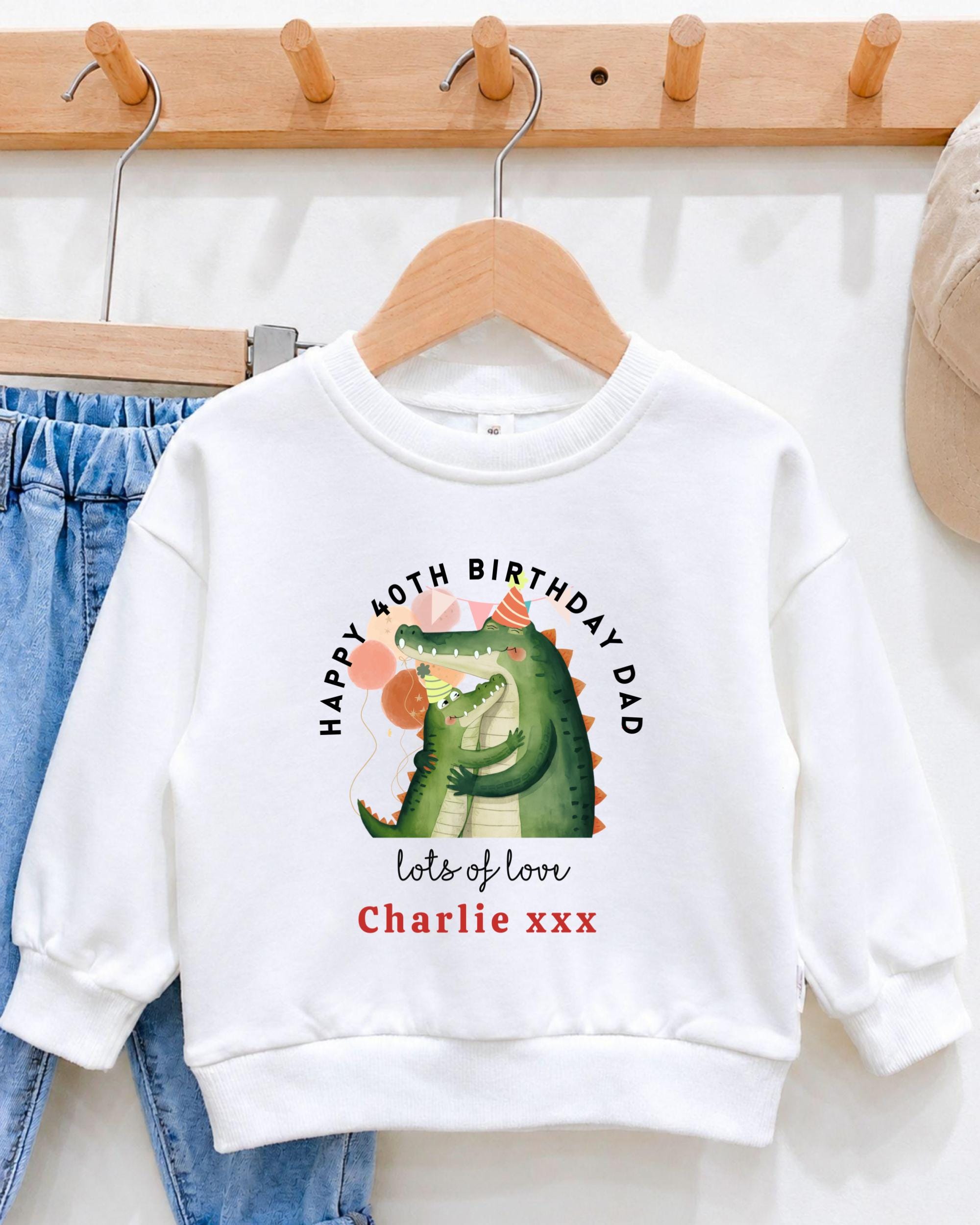 A white sweatshirt with a graphic of a green alligator wearing a party hat and the text "Happy 40th Birthday Dad lots of love Charlie xxx" printed on it.