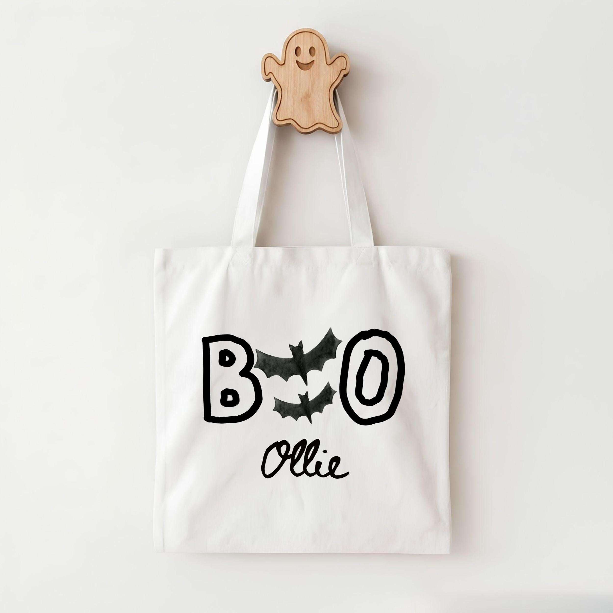 A white tote bag with the text "BOO OLLIE" printed on it, along with bats and a ghost-like figure.