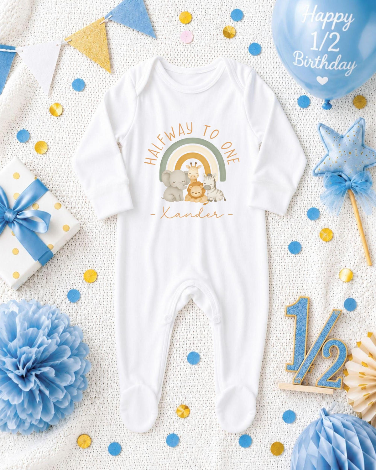 A white onesie with a rainbow graphic and the text "Halfway to one" is displayed among various baby-related items, including a blue balloon, confetti, and a star decoration.