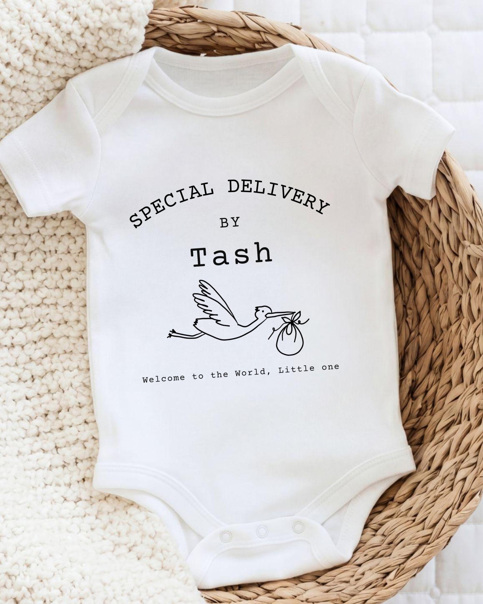 A white baby onesie with text and a graphic design, placed on a woven basket.
