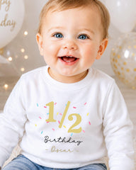 A smiling baby boy wearing a white shirt with the number 1/2 and the text "Birthday Oscar" printed on it.