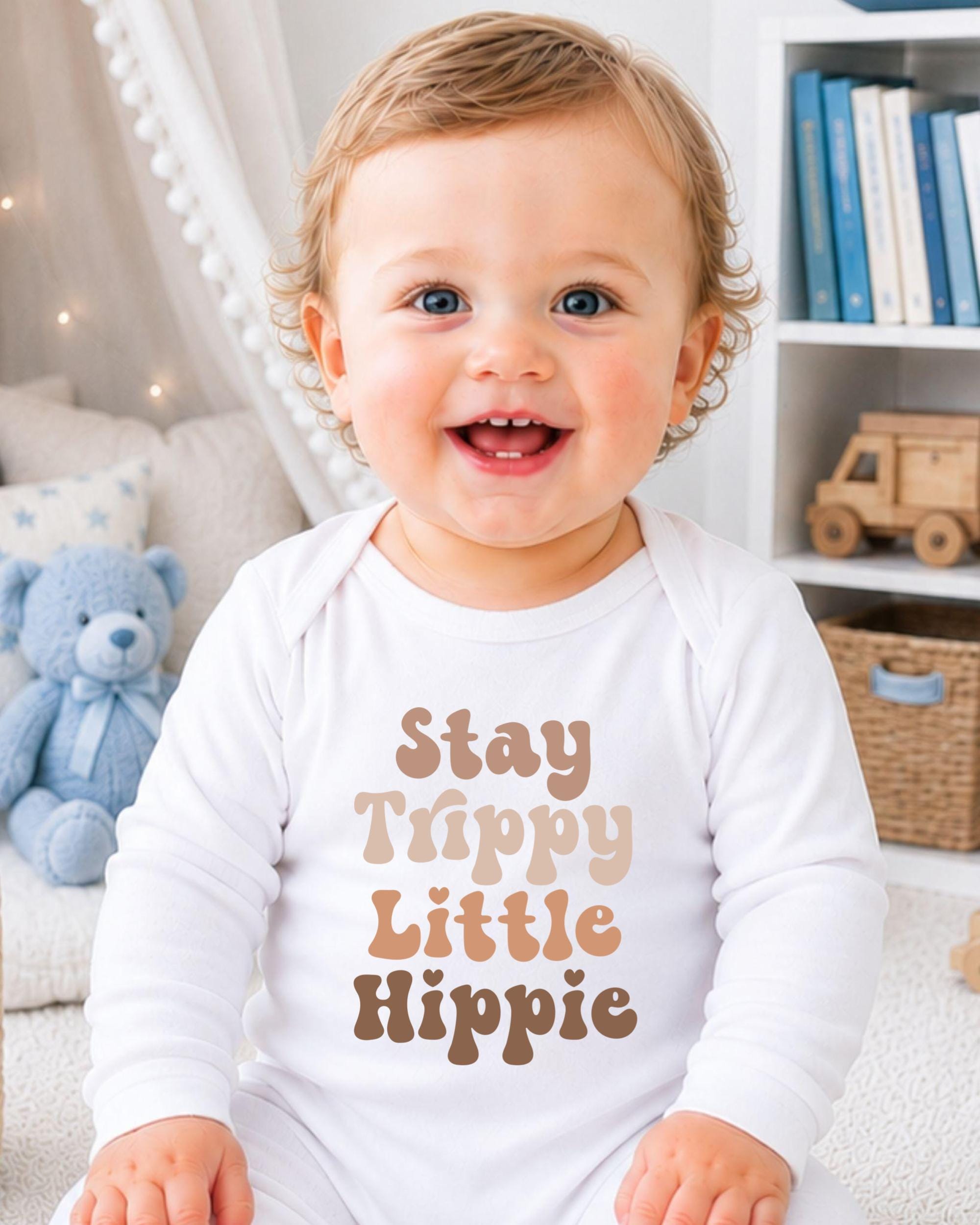 A smiling baby wearing a white onesie with the text "Stay Trippy Little Hippie" printed on it.