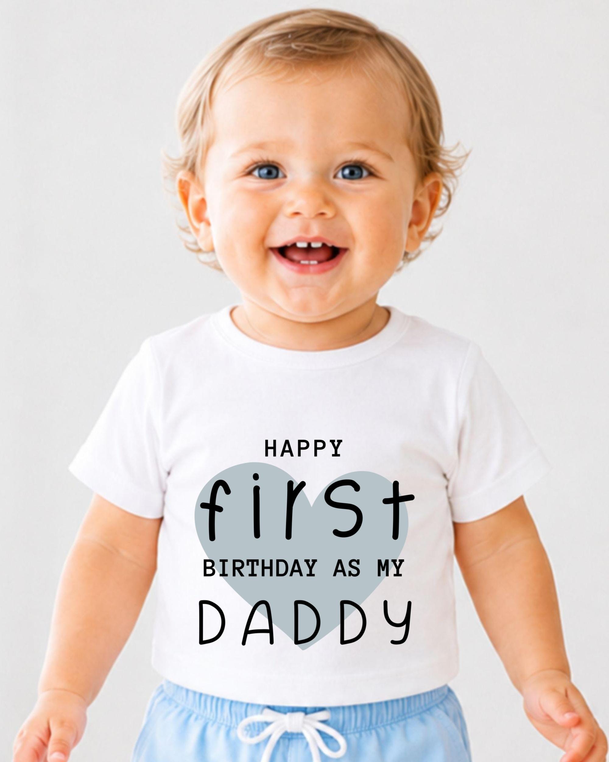 A smiling baby wearing a white t-shirt with text that says "Happy first birthday as my Daddy".