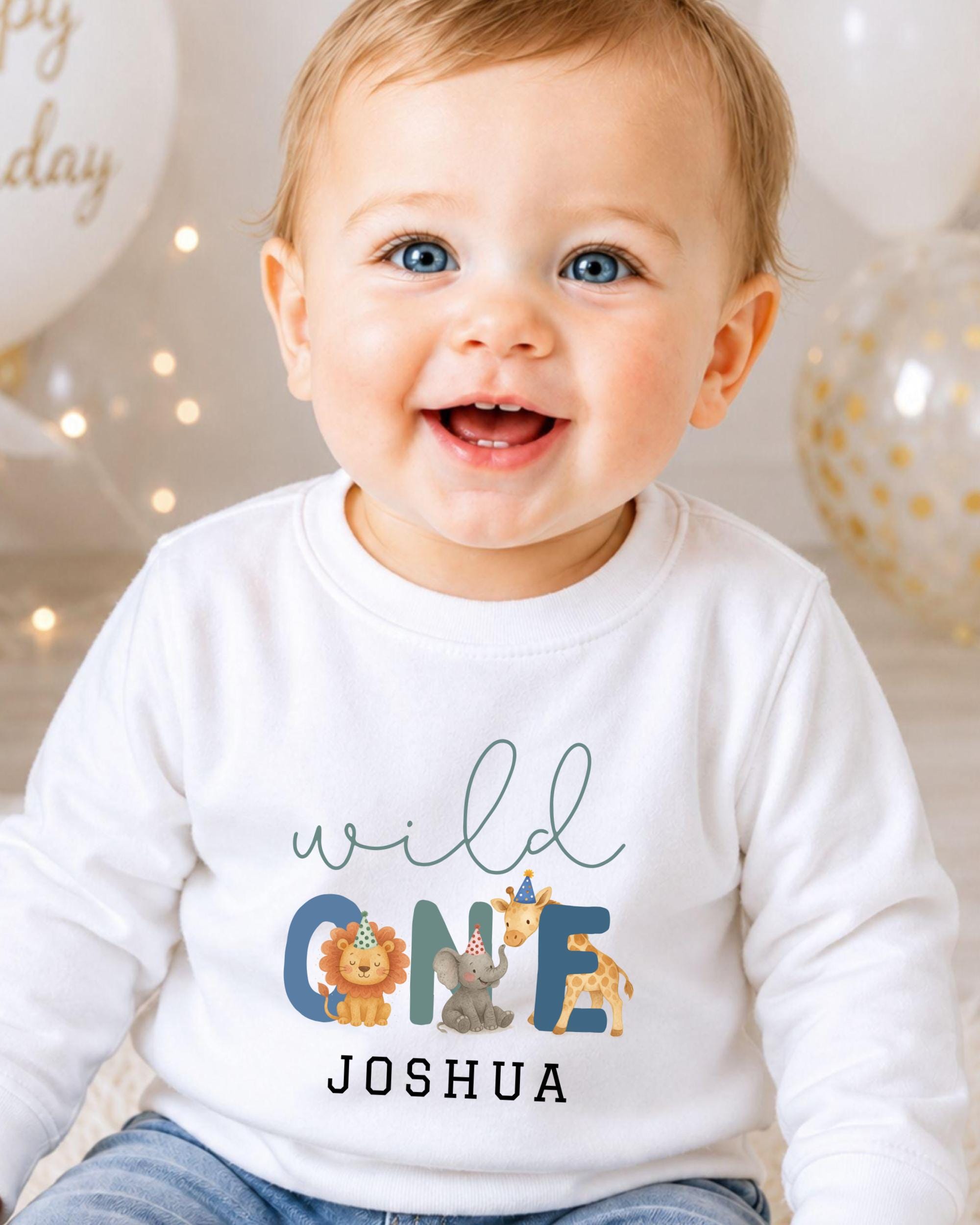 A smiling baby boy wearing a white long-sleeved shirt with a personalized text and animal graphics.