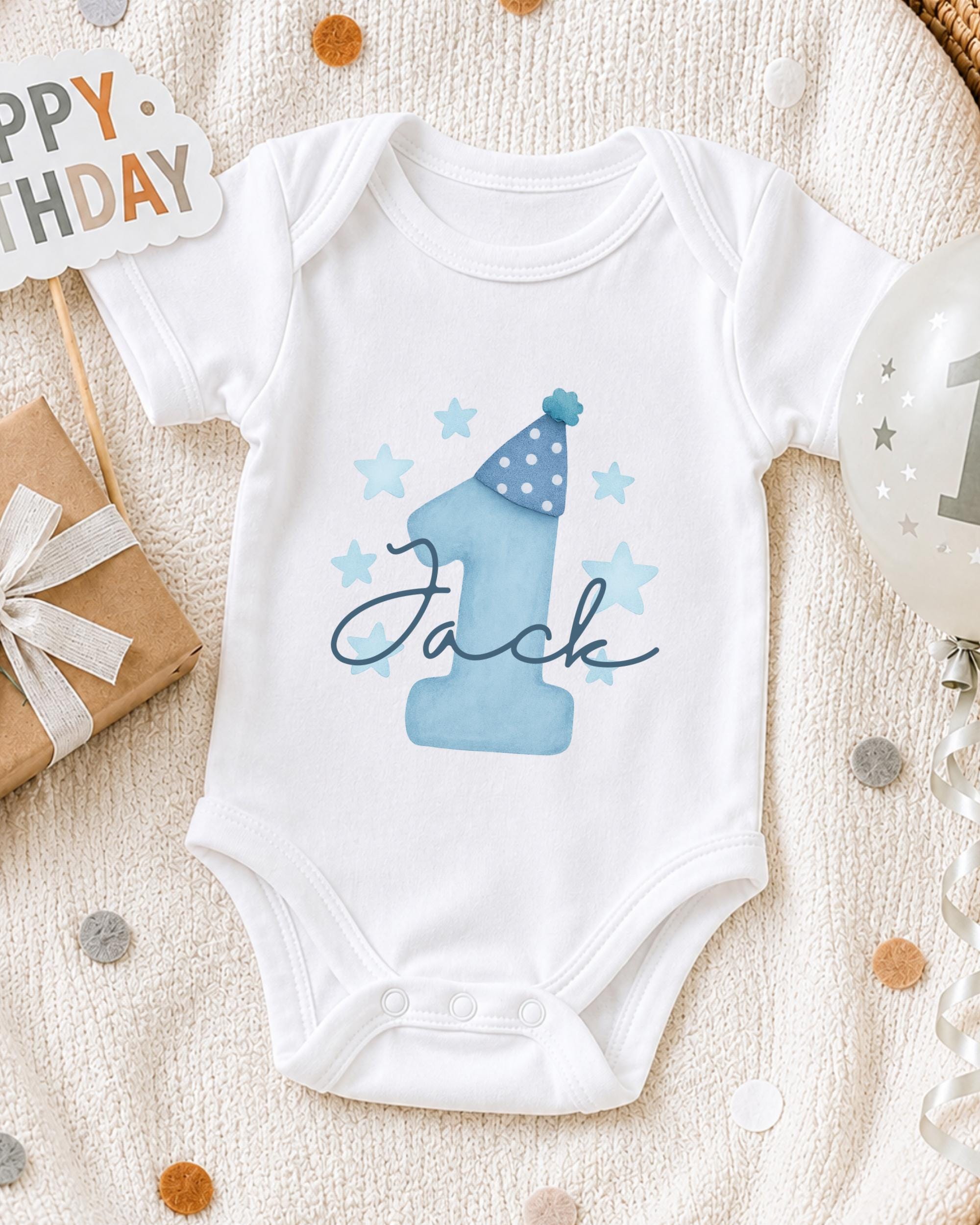A white onesie with a blue number one and stars, along with a "Happy Birthday Jack" sign, is displayed on a white blanket.