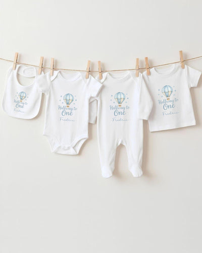 A collection of baby clothes, including onesies and bibs, hanging on a clothesline.