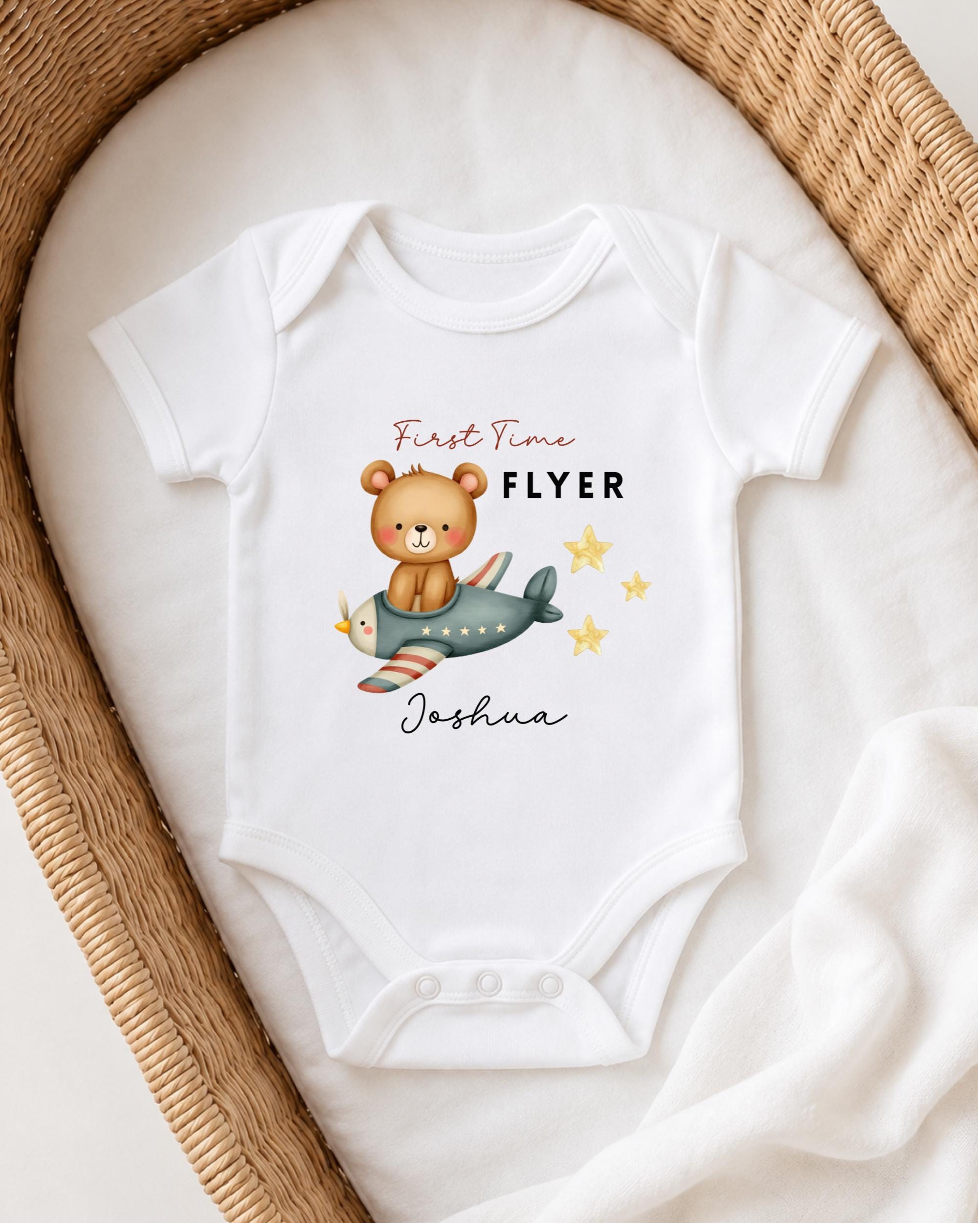 A white onesie with a cartoon bear and airplane printed on it, placed on a white blanket.