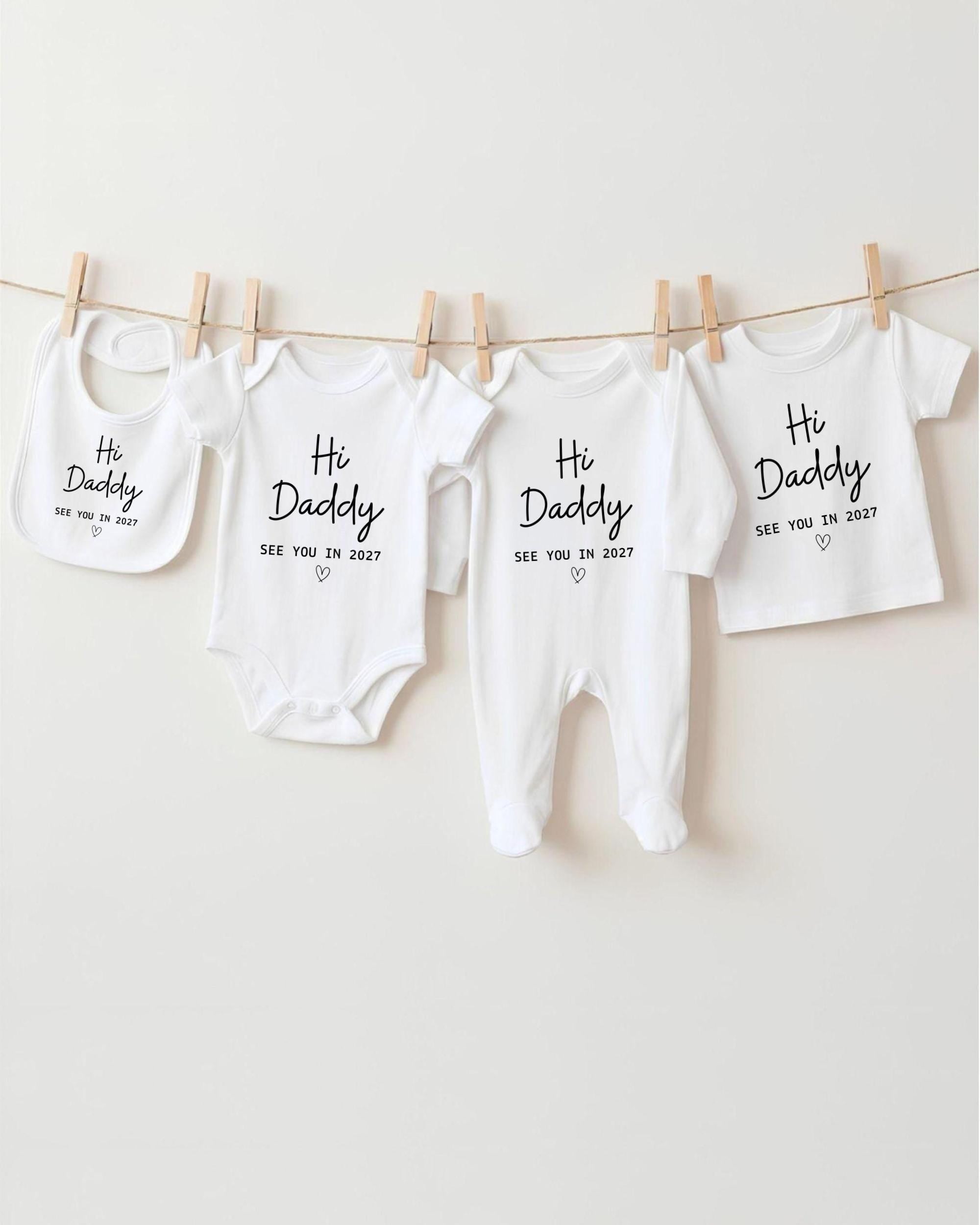 a collection of four white baby clothes hanging on a clothesline, each with a unique message printed on it.