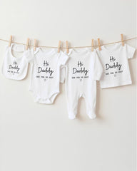 a collection of four white baby clothes hanging on a clothesline, each with a unique message printed on it.