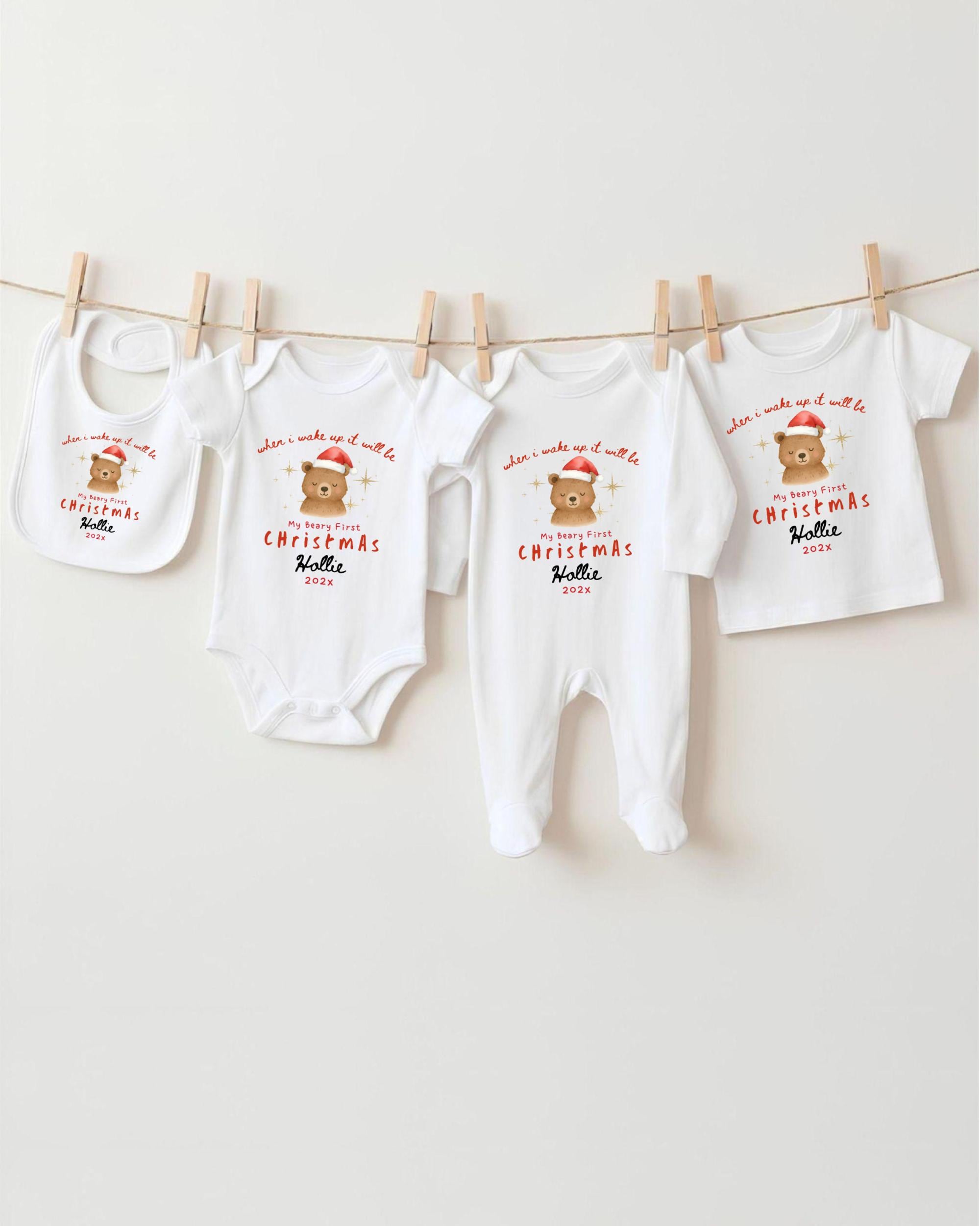 A row of four white Christmas-themed baby clothes, including onesies and bibs, hanging on a clothesline.