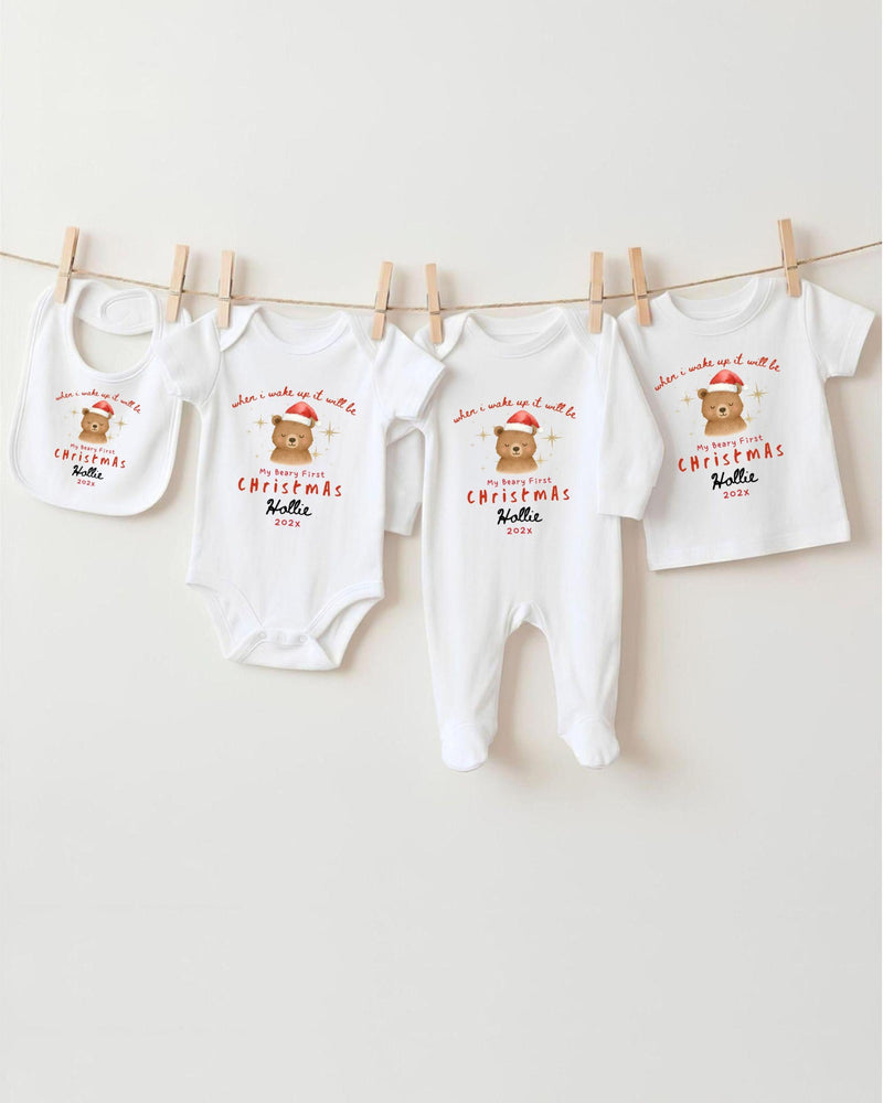 A row of four white Christmas-themed baby clothes, including bodysuits and bibs, hanging on a clothesline.