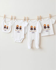 A row of four white baby clothes with the name "Big Cousin Chloe" printed on them, hanging on a clothesline.