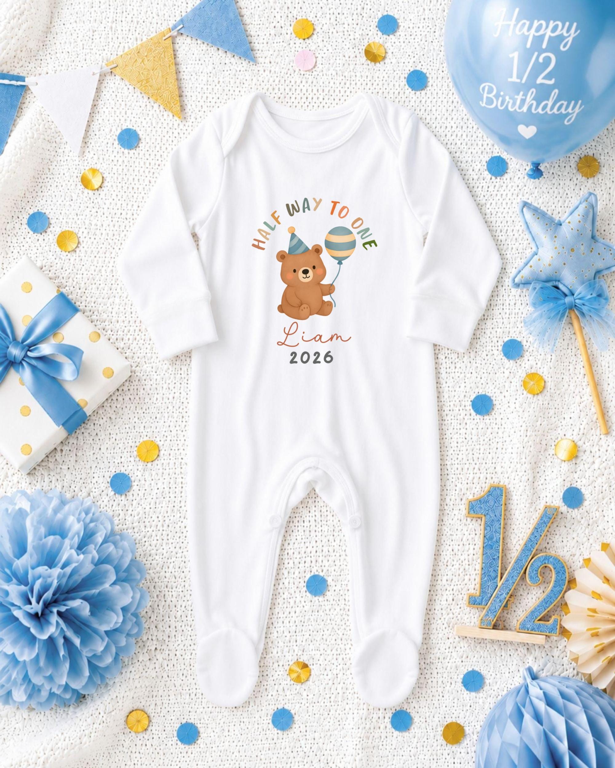 A white onesie with a cartoon bear and the text "Half way to one" is displayed among various baby-related items, including a blue balloon, confetti, and a star decoration.
