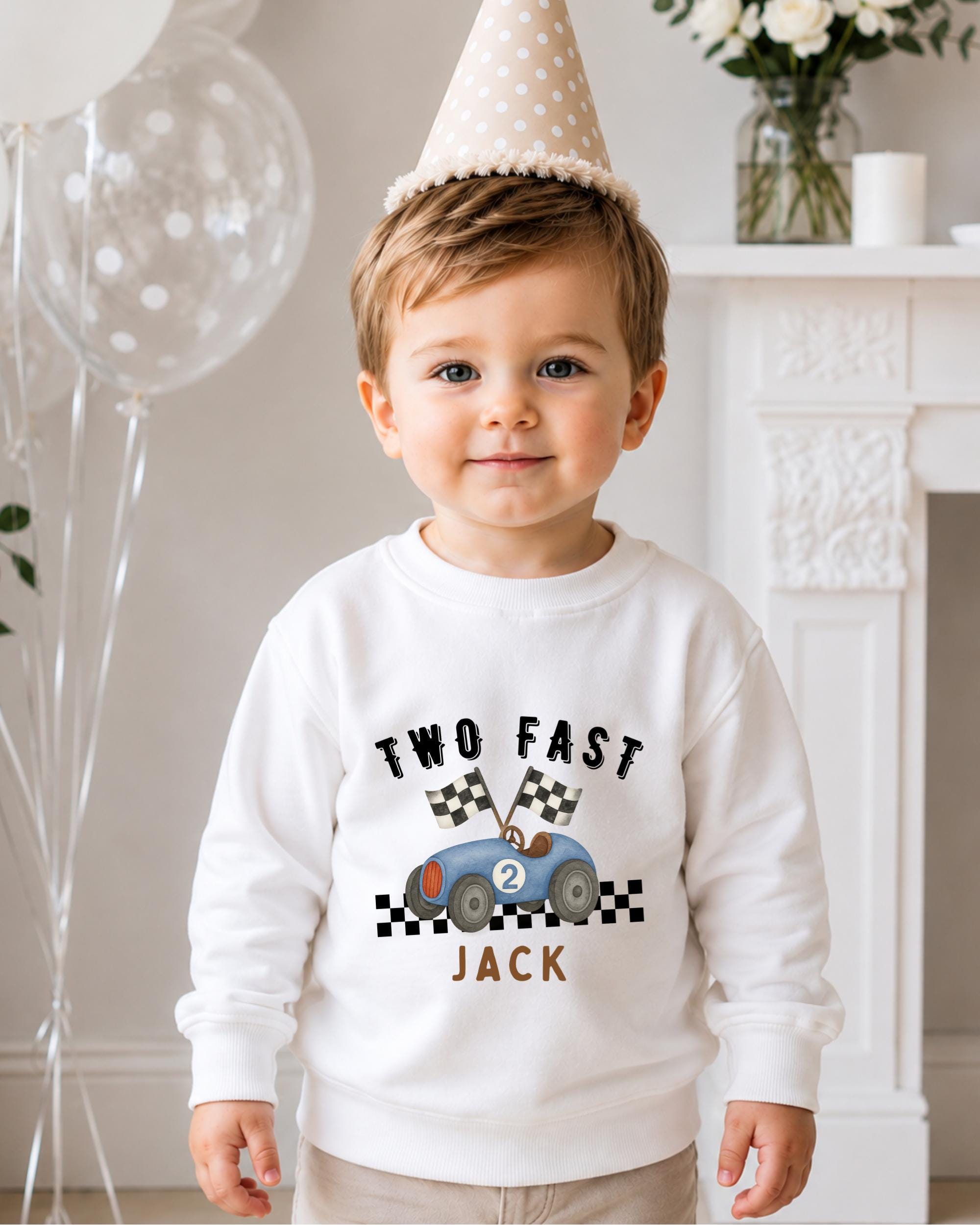 A young boy wearing a white sweatshirt with a cartoon race car and the text "Two Fast Jack" is standing in front of a fireplace.