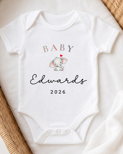 A white baby bodysuit with a small elephant graphic and the text "BABY Edwards 2026" printed on it.