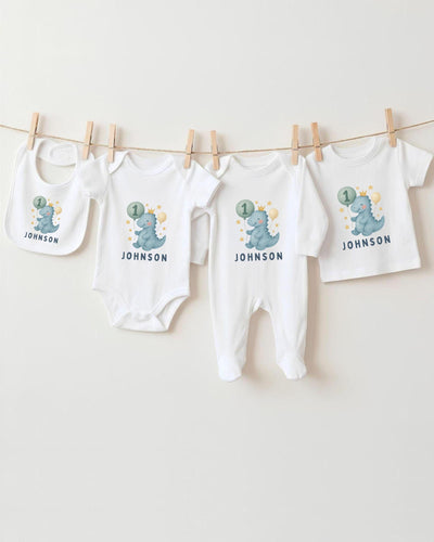 A collection of white baby clothes, including bodysuits and bibs, with dinosaur designs and the name "Johnson" printed on them.