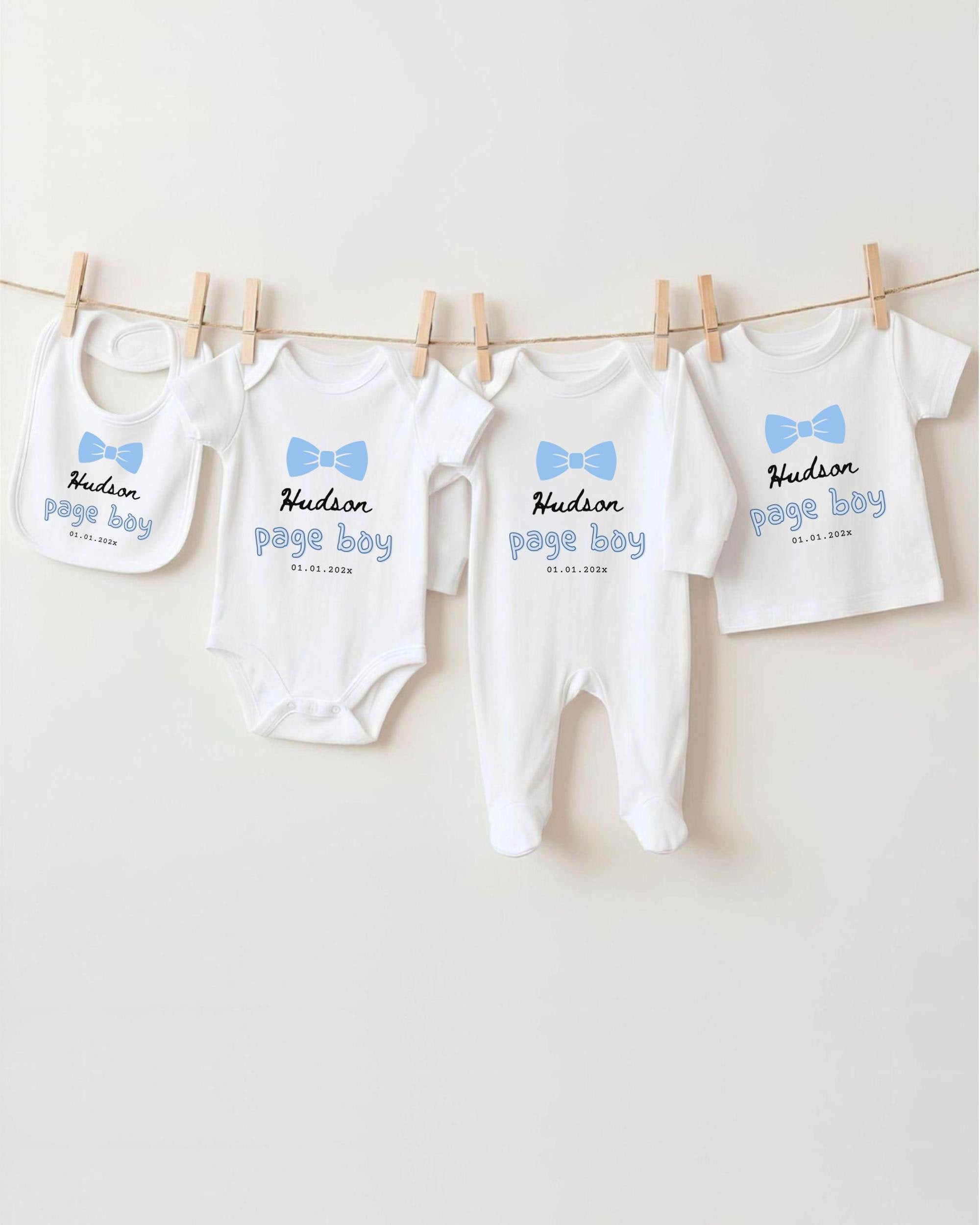 A row of four white baby clothes with blue bows hanging on a clothesline.