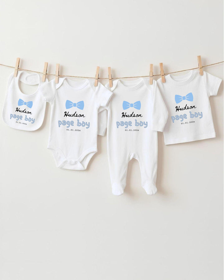 A row of four white baby clothes with blue bows hanging on a clothesline.