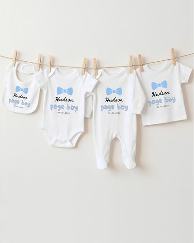 A row of four white baby clothes with blue bows hanging on a clothesline.
