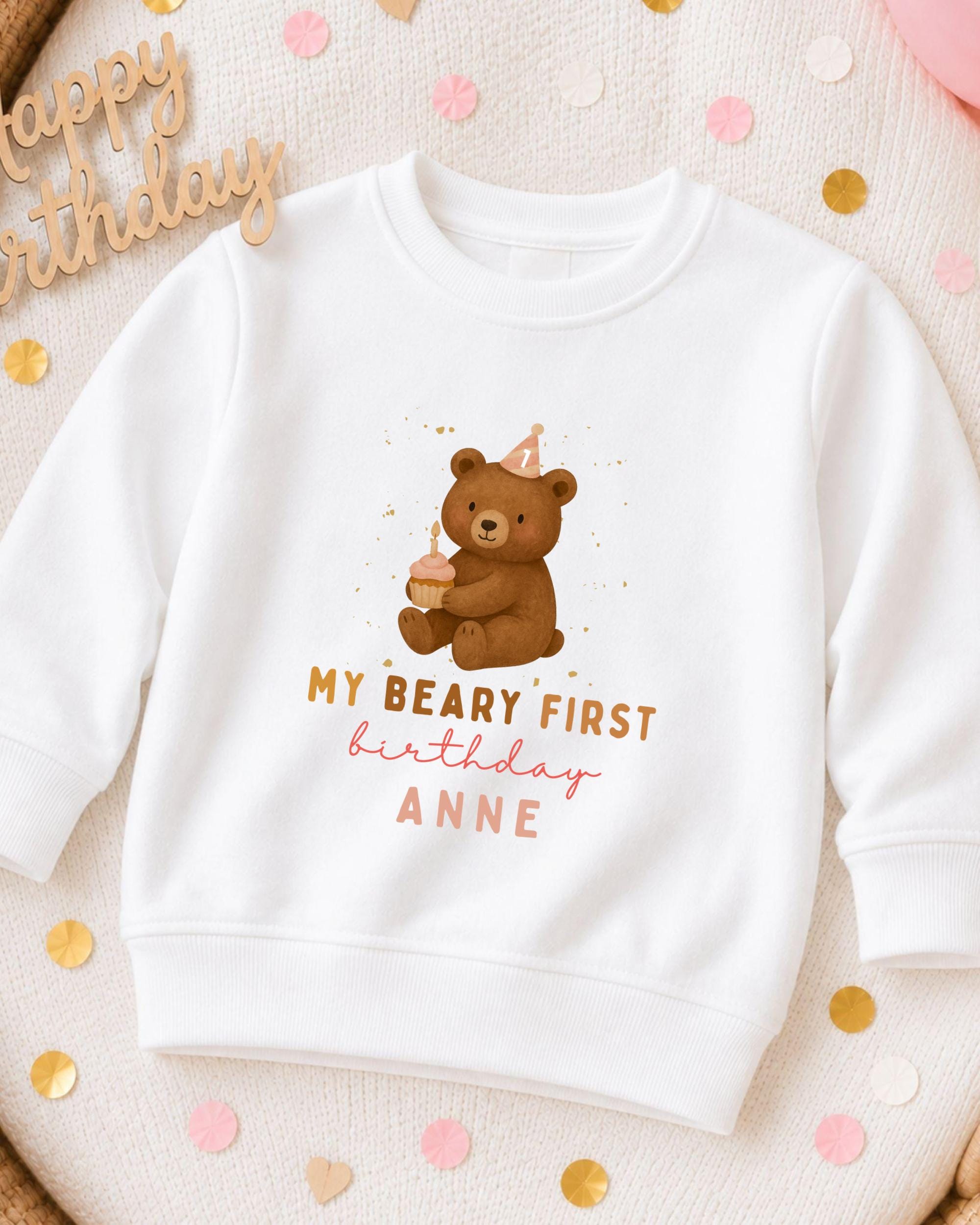 A white sweatshirt with a teddy bear and birthday text printed on it, surrounded by confetti.