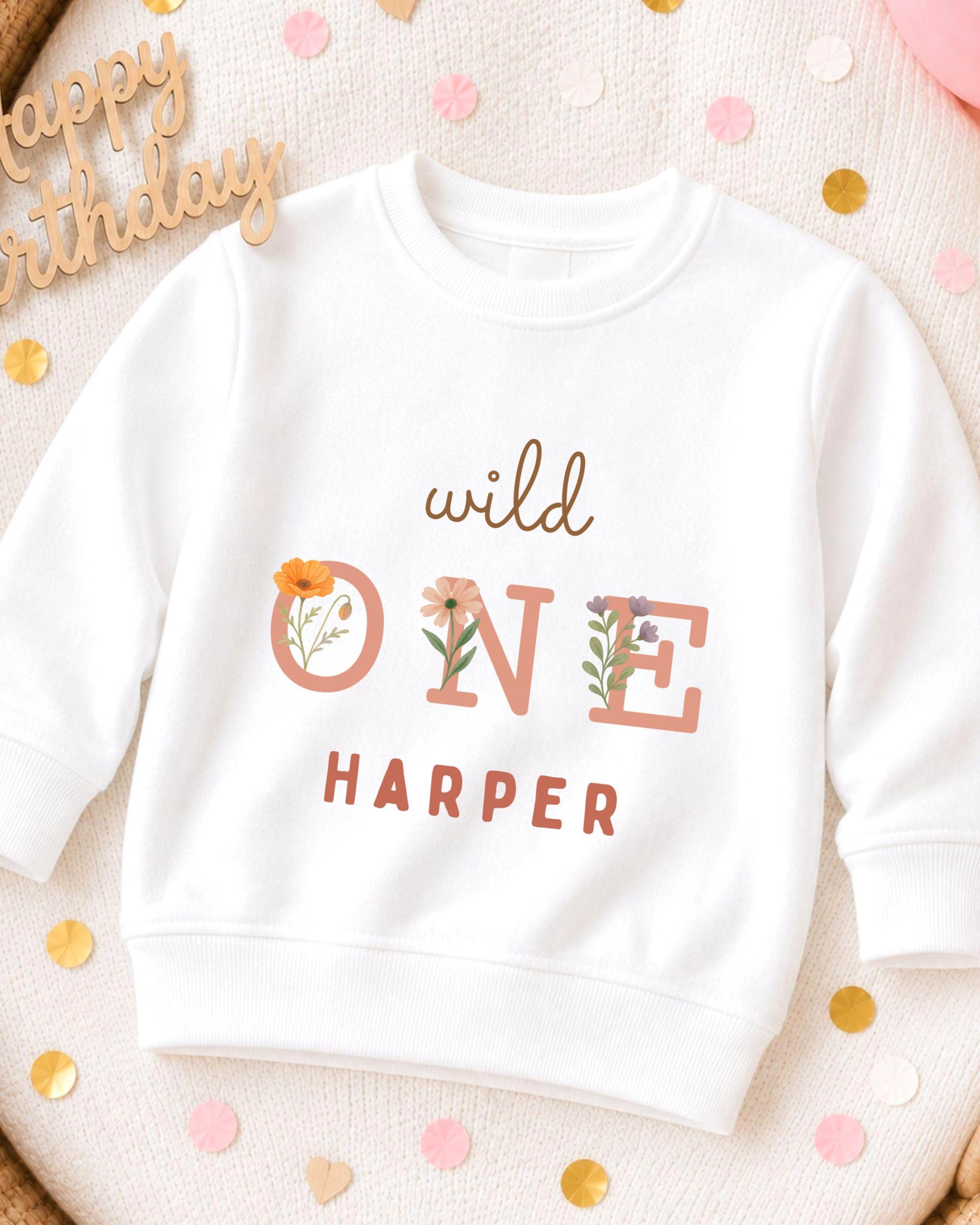 A white sweatshirt with the text "wild one Harper" printed on it, surrounded by confetti.