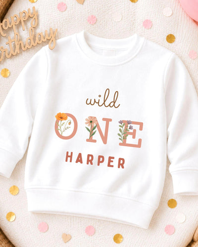 A white sweatshirt with the text "wild one Harper" printed on it, surrounded by confetti.