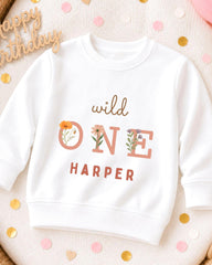 A white sweatshirt with the text "wild one Harper" printed on it, surrounded by confetti.