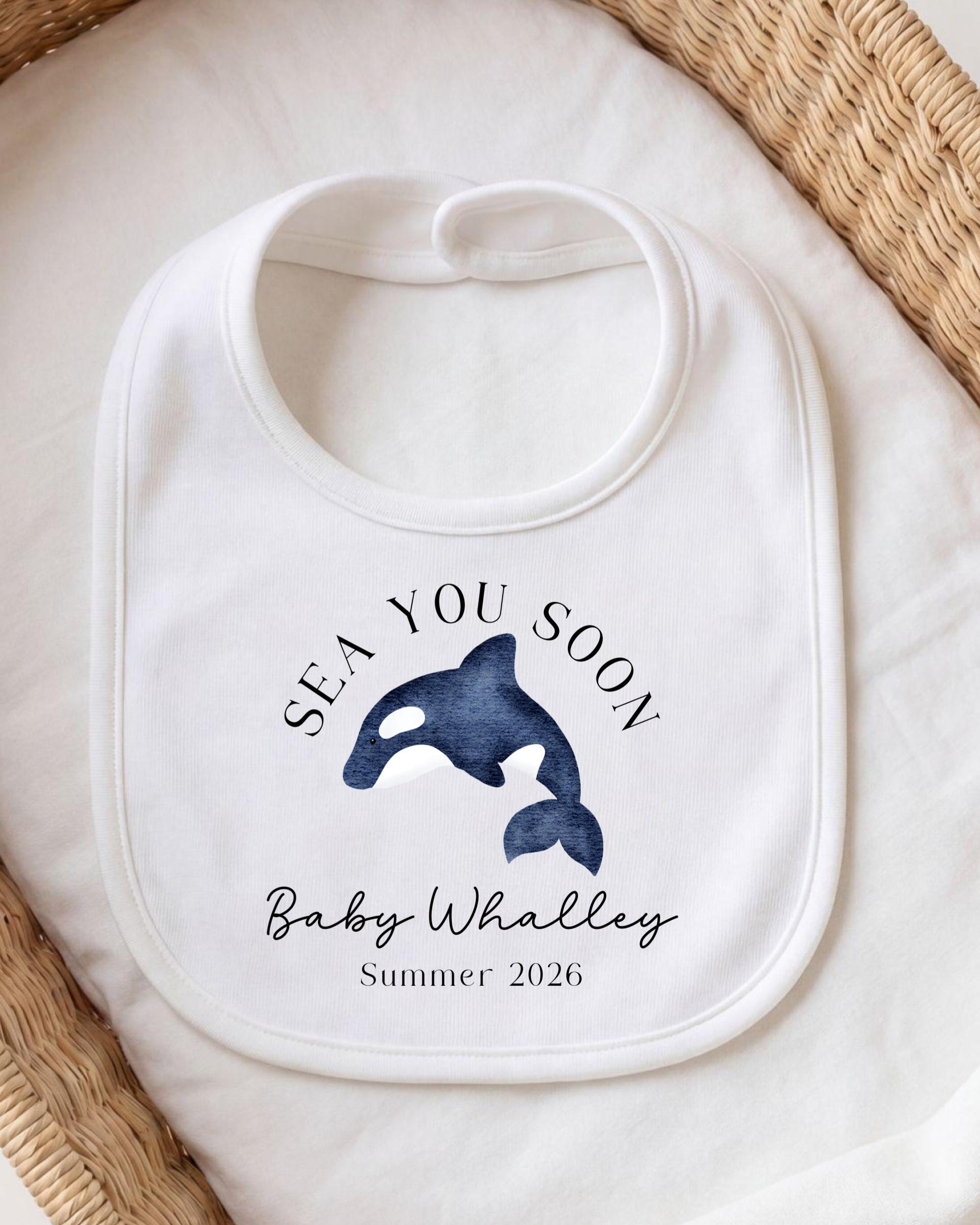 A white bib with a blue whale graphic and text that says "SEA YOU SOON Baby Whallley Summer 2026".