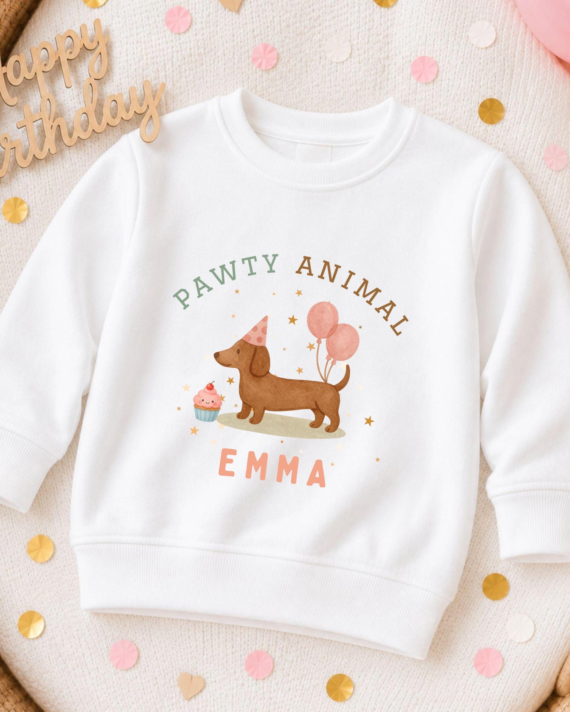 A white sweatshirt with a cartoon image of a dog wearing a party hat and balloons, along with the text "Pawty Animal Emma" printed on it.