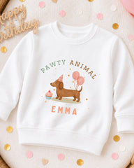 A white sweatshirt with a cartoon image of a dog wearing a party hat and balloons, along with the text "Pawty Animal Emma" printed on it.