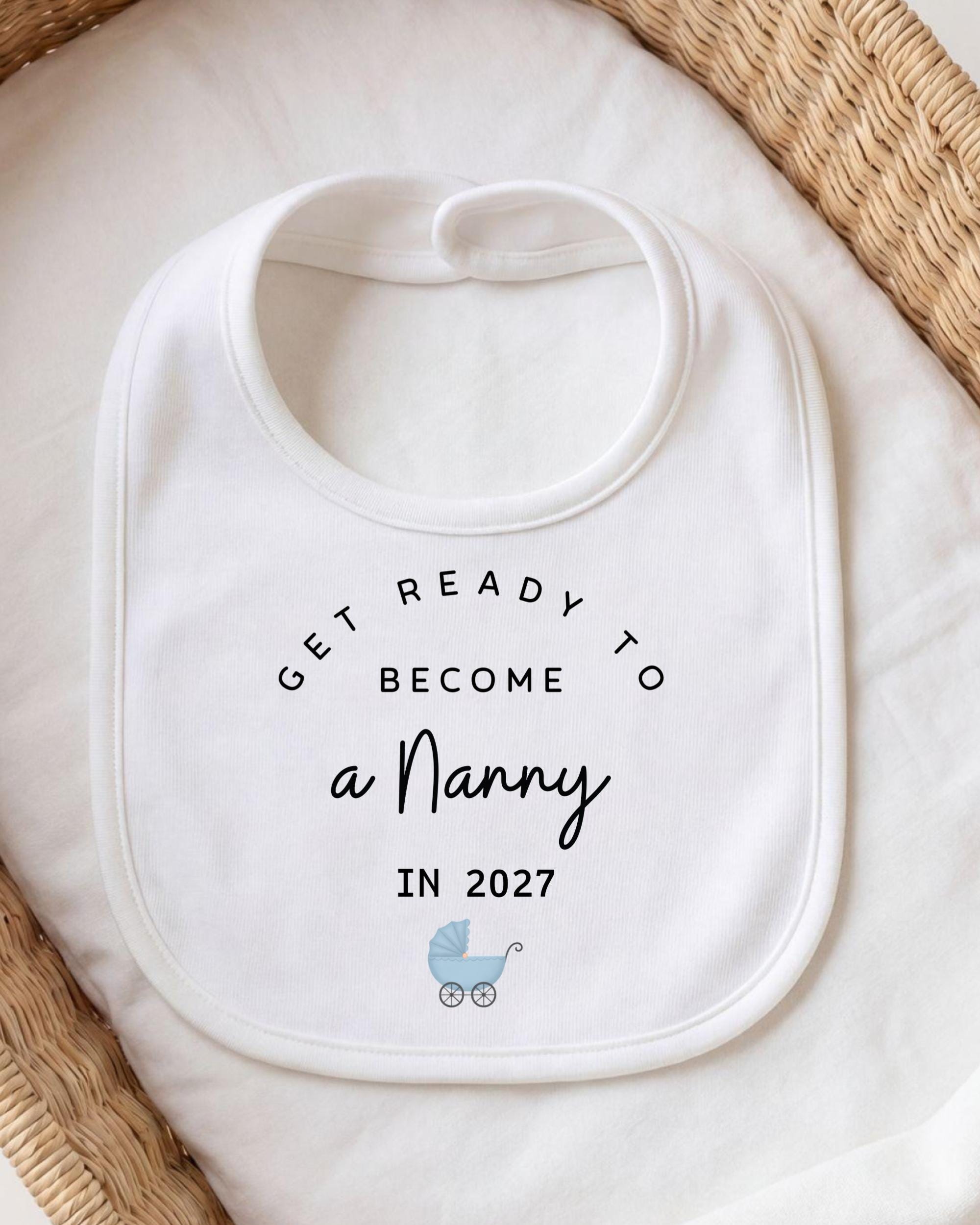 A white bib with the text "GET READY TO BECOME A NANNY IN 2027" printed on it, along with a small illustration of a baby carriage.