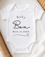 A white baby onesie with the text "Baby Box Born in 2026" printed on it.