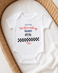 A white onesie with a racing theme, featuring a checkered flag design and text that says "Matching The Race with my Daddy Ellie".