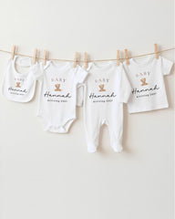 A row of four white baby clothes with the name "Hannah" printed on them, hanging on a clothesline.