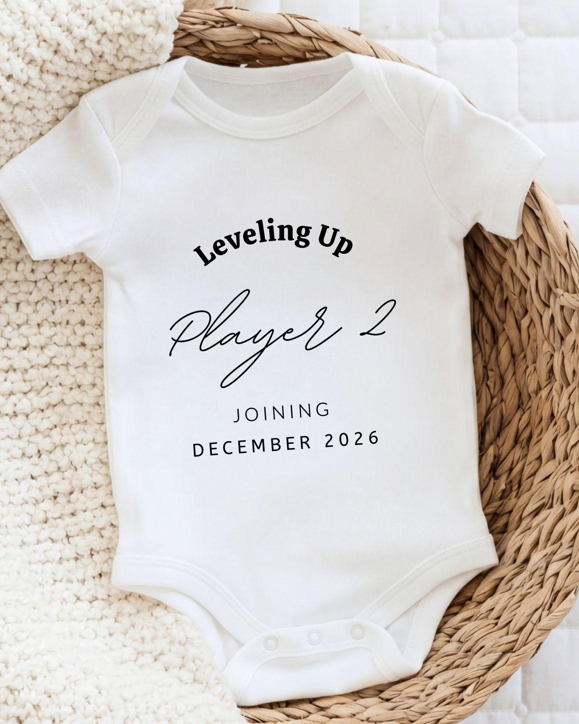 A white baby onesie with text printed on it, placed on a woven basket.