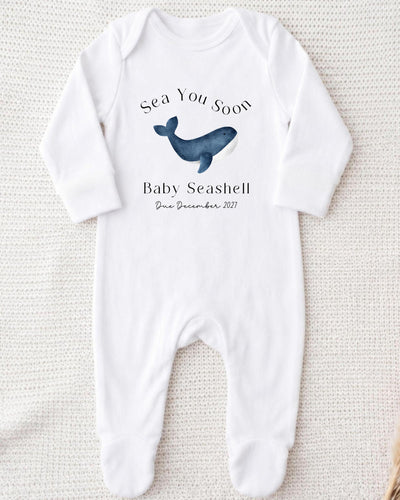 Personalisable white Baby Grow with a blue watercolour whale between black 'Sea You Soon' and 'Baby Seashell Due December 2027' lettering.