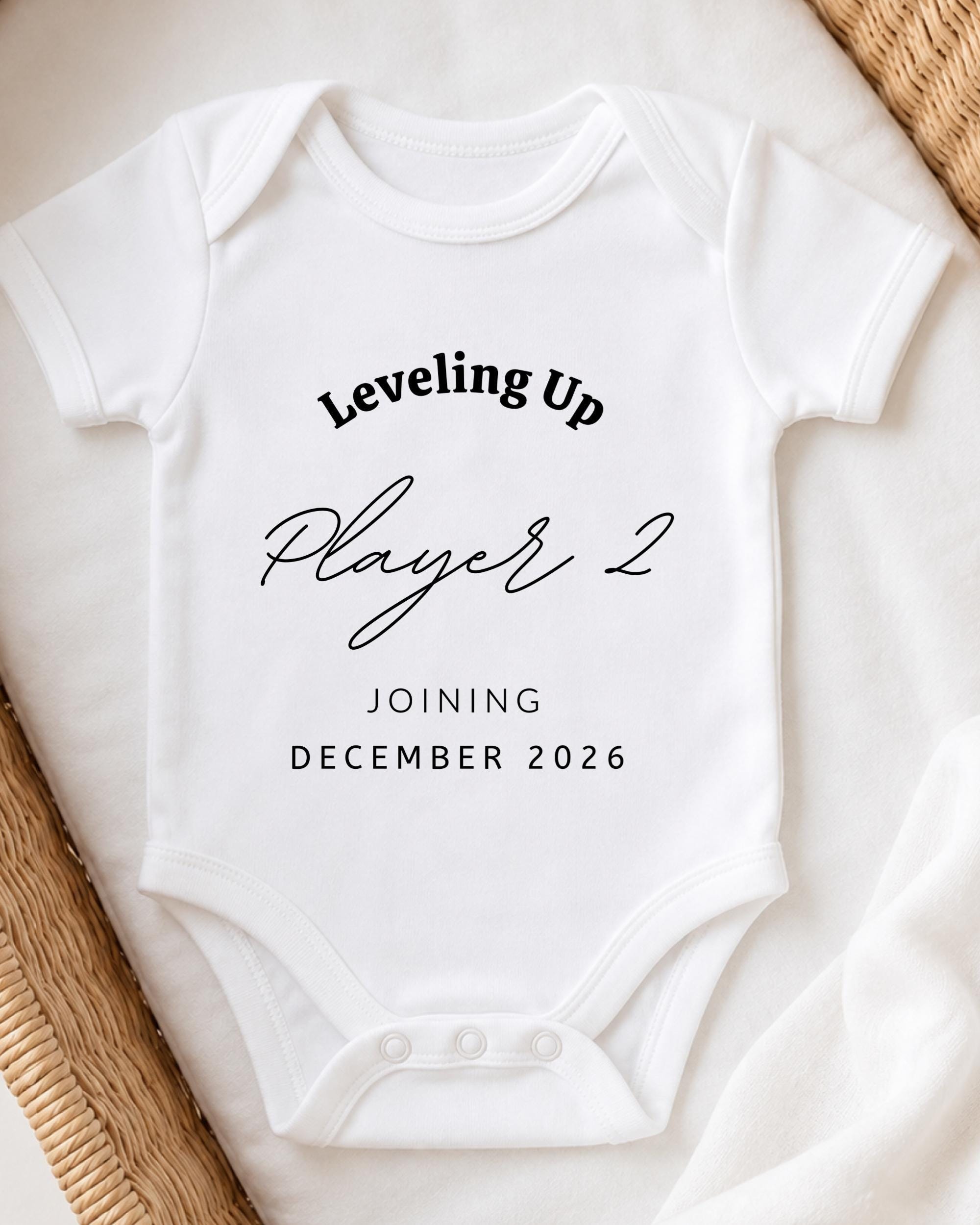 A white baby onesie with text printed on it, placed on a white surface.