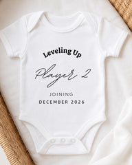 A white baby onesie with text printed on it, placed on a white surface.